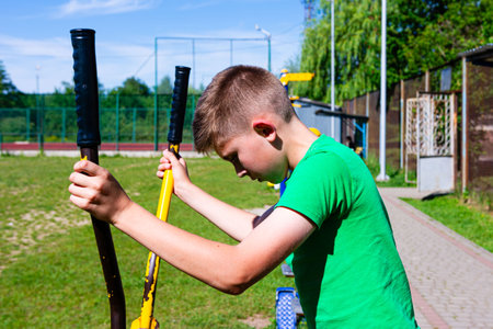 A young boy uses outdoor exercise equipment. He's wearing a green shirt and appears focused on his workout. The setting is a sunny park.の写真素材