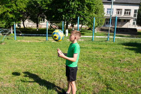 A boy skillfully juggles a soccer ball in a grassy park near playground equipment. The sun shines brightly, creating a joyful and active scene.の写真素材