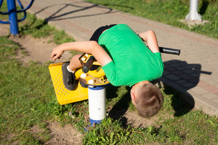 A young boy playfully hangs upside down on yellow playground equipment. He is wearing a green shirt and appears to be having fun in a park setting.の写真素材
