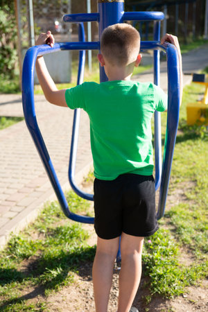A child uses outdoor gym equipment, focusing on upper body strength. The sunny day and green surroundings create a healthy atmosphere.の写真素材