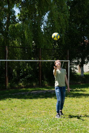 A young person joyfully catches a ball against a backdrop of lush greenery and a partially visible soccer goal. A bright, sunny day.の写真素材