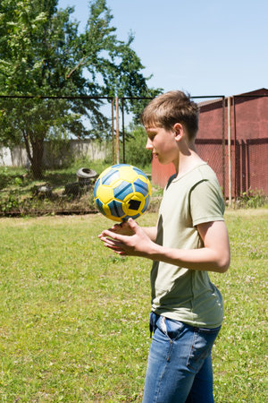A teenage boy practices his soccer ball skills outside. He's wearing a light green shirt and jeans, focused on juggling the ball.の写真素材