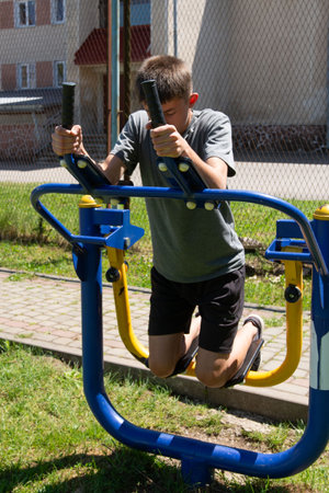 A young person engages in a workout using outdoor gym equipment. The setting appears to be a park or public space, sunny and outdoors. The focus is on physical activity and fitness.の写真素材