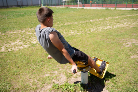 A young man engages in an outdoor workout, utilizing a public fitness machine. He is focused on his exercise in a sunny park-like setting.の写真素材