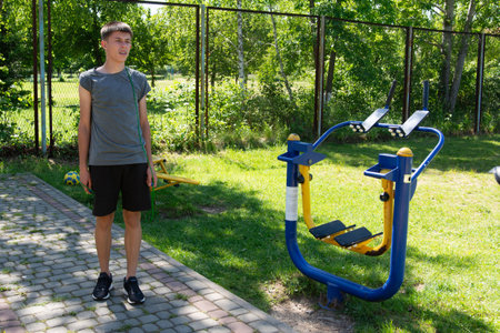 A young man stands near a blue and yellow outdoor exercise machine. Jump rope exercises on the sports field.の写真素材