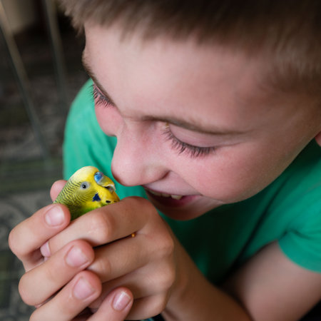 A young boy cradles a small parrot in his hands, his face expressing gentle affection. The scene is...