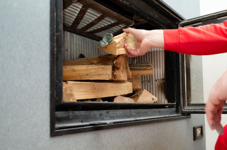 Hands skillfully arrange pieces of wood inside a sleek wood stove, infusing the contemporary living space with warmth and inviting aromas on a cool afternoon.の写真素材
