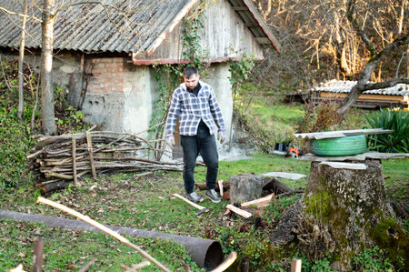 Amidst a serene landscape, a man skillfully works with wood, demonstrating craftsmanship. The warm afternoon light highlights his focus and the rustic charm of the setting.の写真素材