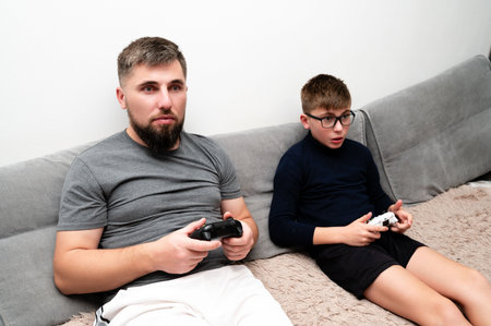 Two players are focused on their gaming experience, sitting closely together on a comfortable couch with controllers in hand, enjoying quality time on a weekend.の写真素材