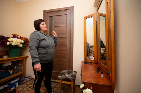 A woman stands in a warm-toned room, interacting with her reflection in a wooden mirror, surrounded by a mix of vibrant flowers and homey furniture, creating a serene atmosphere.の写真素材