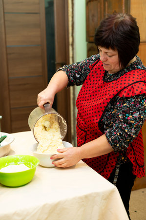 A skilled cook pours prepared dough into a bowl, wearing a cheerful apron while focusing on the art of making traditional dumplings in a warm kitchen.の写真素材