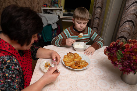 In a heartwarming kitchen setting, a grandmother delights in sharing her homemade desserts with her young grandson as they spend a cozy afternoon together with warm smiles.の写真素材