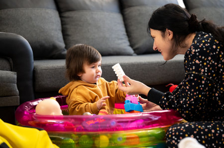 A joyful interaction unfolds as a caregiver and a young child play together. The vibrant inflatable pool is filled with colorful toys, creating a delightful environment.の写真素材