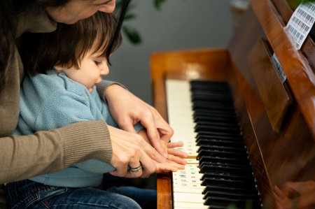 A young child joyfully plays the piano, fingers guided by a caring adult, immersed in the sounds of music on a bright afternoon in a welcoming home environment.の写真素材