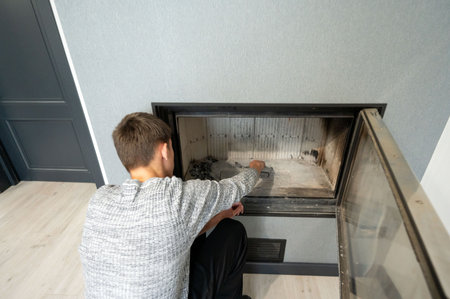 A person carefully cleans ash and debris from a stylish fireplace, ensuring it remains functional and aesthetically pleasing, perfect for a comfortable winter day.の写真素材