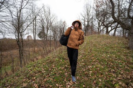 A young person strolls along a grassy hill covered with fallen leaves, dressed warmly for the cool weather, embracing the serene beauty of an autumn day.の写真素材