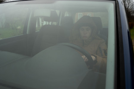 A young individual sits behind the wheel of a parked vehicle, surrounded by thick fog on an overcast day, creating an atmosphere of solitude and contemplation.の写真素材