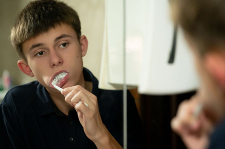 A young boy stands in front of a mirror, focusing on brushing his teeth. Soft morning light illuminates the bathroom, creating a calm and serene atmosphere for his routine.の写真素材