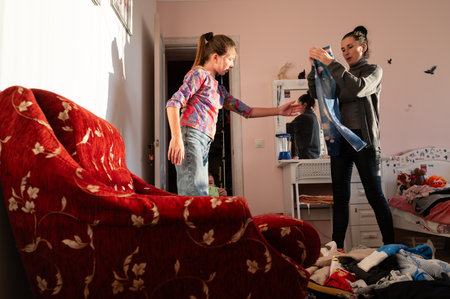 Two young women are joyfully sorting through clothes in a cozy bedroom filled with warmth, laughter, and rays of afternoon sunlight streaming through the window.の写真素材