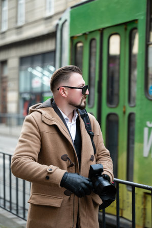 A fashionable individual holds a camera, observing the vibrant street life while a green tram passes...