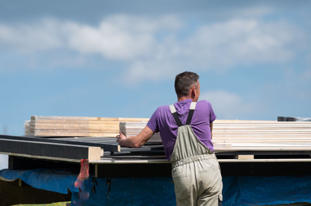 A worker carries white-painted wooden boards for the installation of a gazebo, the work is taking...