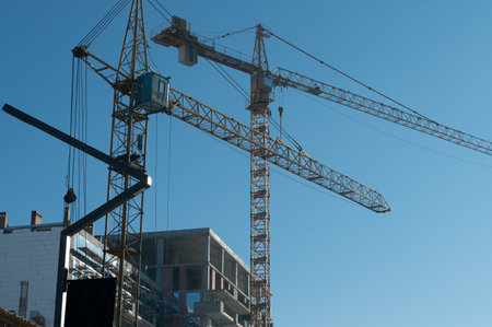 Multiple construction cranes tower above a developing structure in a bustling urban area,...