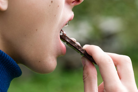 Close-up of a person taking a bite of a chocolate bar. The focus is on the treat and the action of enjoying a sweet snack.の写真素材