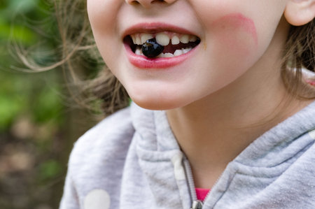 Close-up of a child with a dark berry between their teeth. They appear to be enjoying a snack in a natural outdoor setting.の写真素材