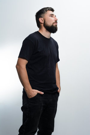 Man in black shirt and jeans, hands in pockets, looking to the side.