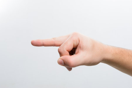 Close-up of a hand with extended index finger pointing towards the left side against a clean white backdrop. The focus is on the gesture.の写真素材