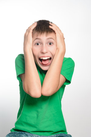 A portrait of a surprised teenage boy. He's wearing a green shirt and has his hands on his head. His expression is one of disbelief or amazement.の写真素材