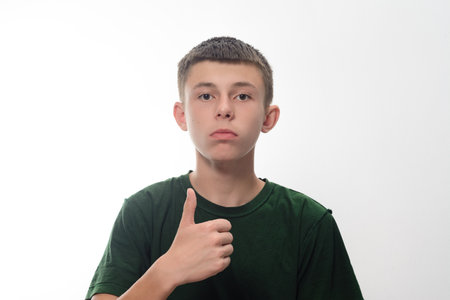 A young teenage boy with short brown hair gives a thumbs-up gesture against a plain white background. He's wearing a dark green t-shirt.の写真素材
