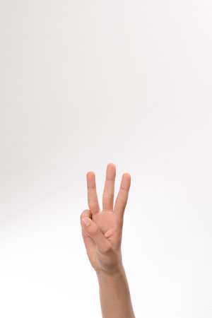 A detailed image of a person's hand displaying the number three. The hand is positioned against a clean white backdrop, providing a clear and simple visual.の写真素材