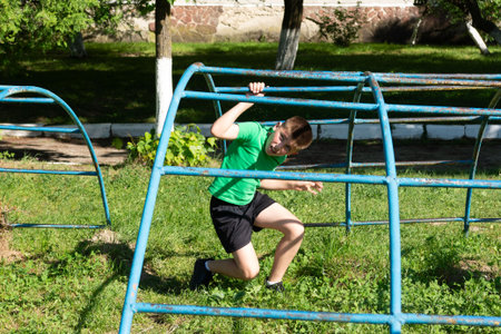 A young boy actively engages with a blue metal climbing frame in a grassy park. He appears playful...