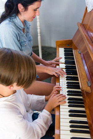 A young girl receives piano instruction from a woman. The child's hands are positioned on the keys, guided by the adult. The setting is a bright, simple room.の写真素材