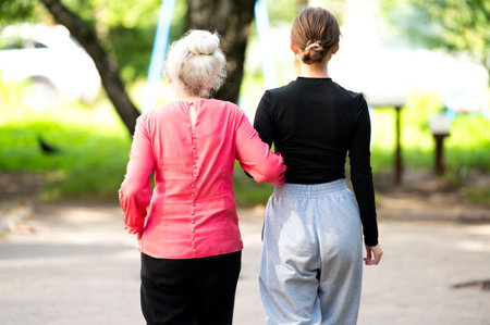 Amidst the greenery, two women stroll closely, relishing a moment of connection and warmth, as the sun filters through the trees, creating a serene atmosphere.の写真素材