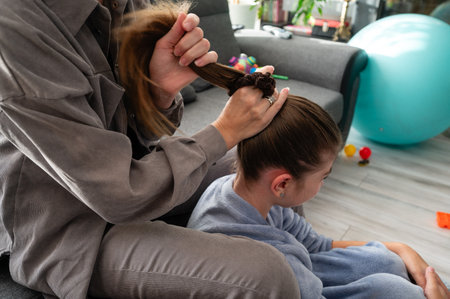 A warm domestic scene unfolds as a parent styles their child's hair, creating a lovely bond filled...