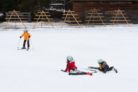 Children enjoy their first skiing experience, laughing and learning on soft snow while wooden ski racks stand proudly in the background on a chilly winter day.の写真素材