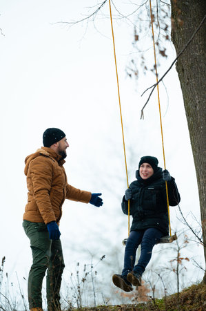 A heartwarming winter scene of a father and child enjoying a swing. The child, bundled in warm clothes, swings happily while the father watches with a smile,の写真素材