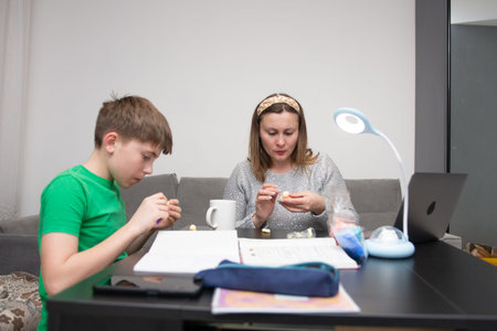 A boy and his mother are joyfully crafting at a table in a modern living room, focused on their...