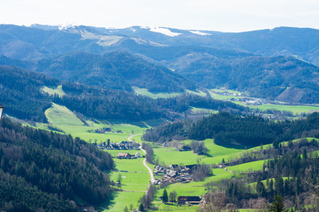 Rolling hills blanketed in lush greenery stretch towards the horizon, where majestic snow-capped peaks rise, embodying a serene spring landscape filled with tranquility.の写真素材