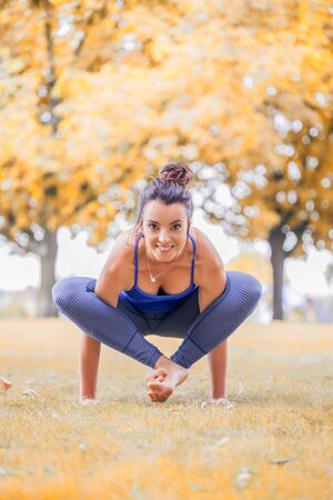 Young woman practicing yoga in the park on the green grass with fallen leaves in autumn with blurred background. Shallow depth of field, vintage imageの写真素材