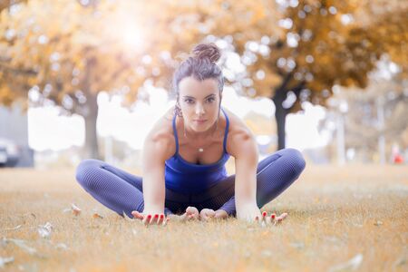 Young woman practicing yoga in the park on the green grass with fallen leaves in autumn with blurred...