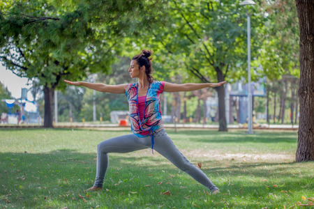 Young woman practicing yoga in the park on the green grass with fallen leaves in autumn with blurred background. Shallow depth of fieldの写真素材