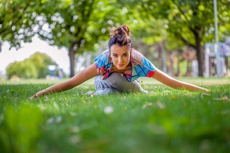 Young woman practicing yoga in the park on the green grass with fallen leaves in autumn with blurred background. Shallow depth of fieldの写真素材