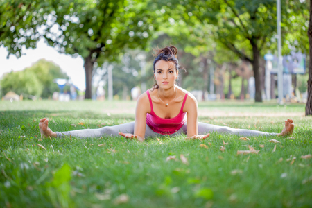 Young woman practicing yoga in the park on the green grass with fallen leaves in autumn with blurred background. Shallow depth of fieldの写真素材