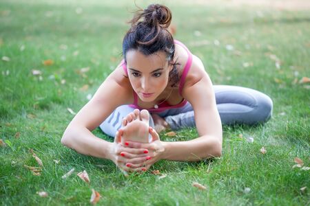 Young woman practicing yoga in the park on the green grass with fallen leaves in autumn with blurred background. Shallow depth of fieldの写真素材