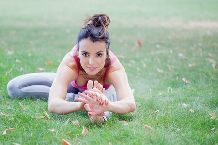 Young woman practicing yoga in the park on the green grass with fallen leaves in autumn with blurred background. Shallow depth of fieldの写真素材