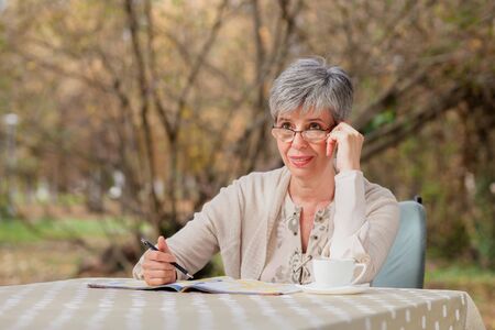 Older woman with gray hair sitting outside in the park and solves sudokuの写真素材
