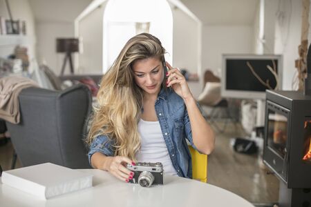 Indoor smiling lifestyle portrait of pretty young woman with camera spaks on the mobile phoneの写真素材
